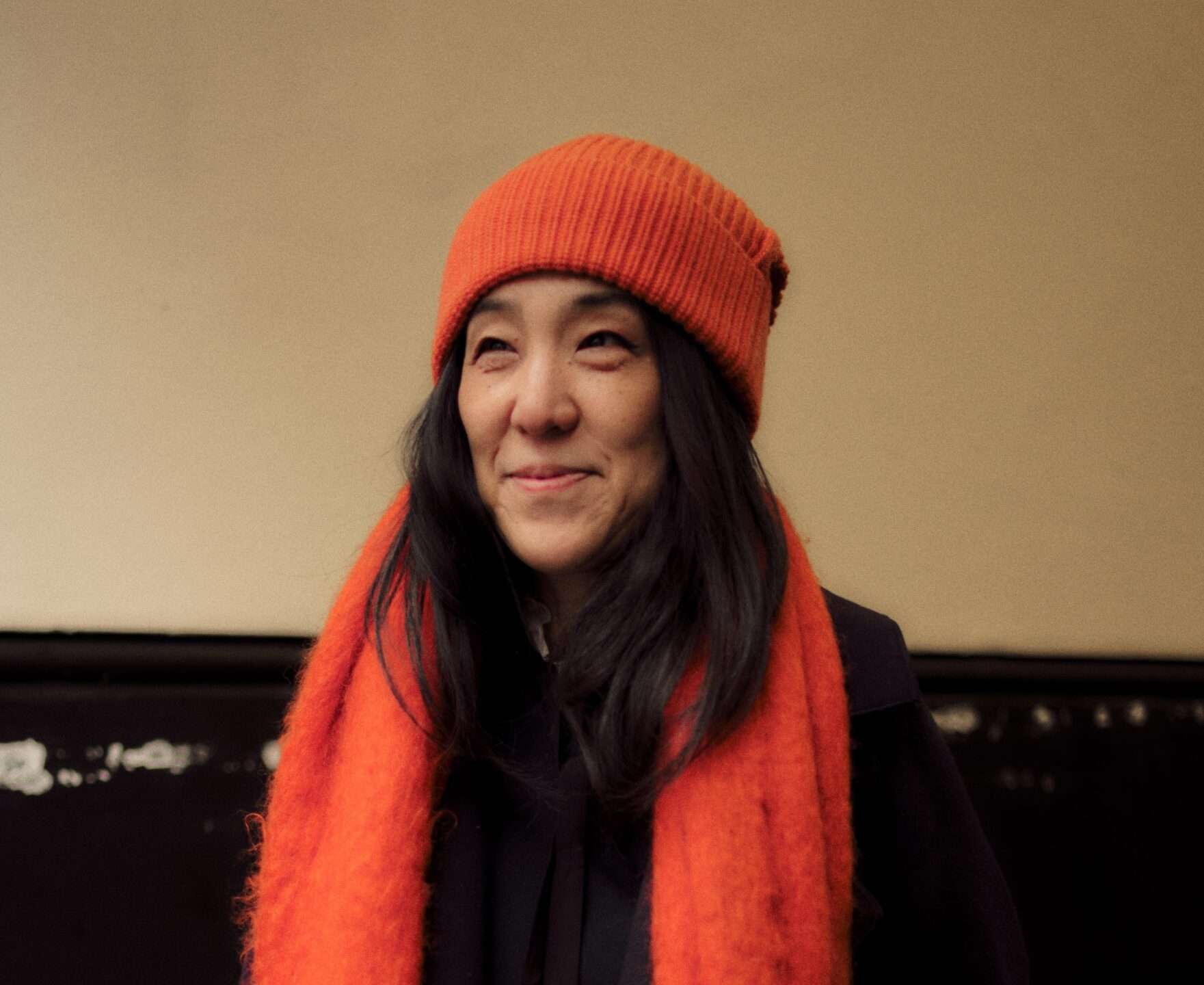 Photograph of Yuki Sumner wearing a red hat and scarf, smiling into the distance